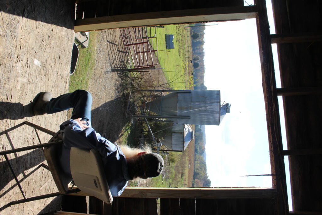 A man sits in a barn looking out at his farm.